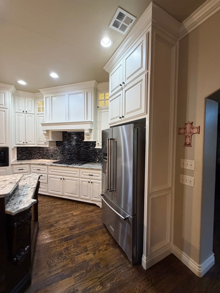Modern kitchen with white cabinetry, stainless steel refrigerator, black tile backsplash, and wood flooring