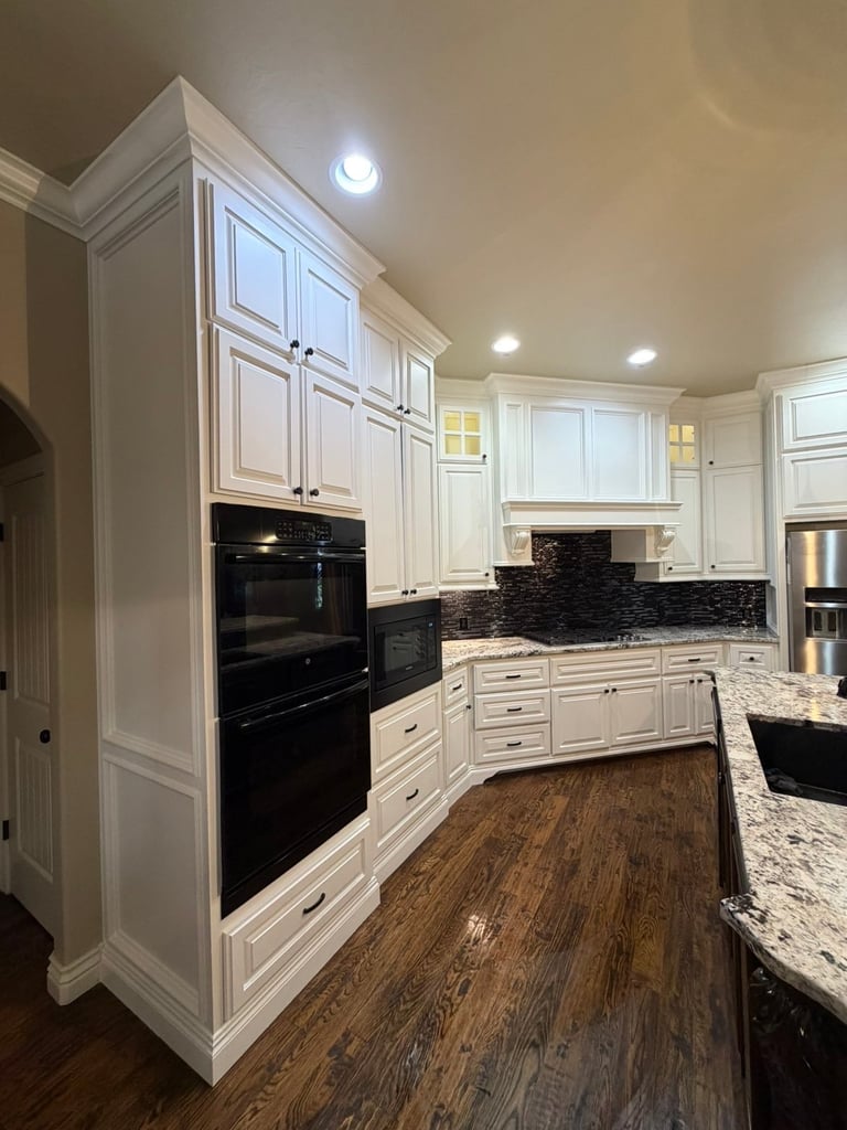 Modern kitchen with white cabinets, black backsplash, granite countertops, stainless steel appliances, and dark wood flooring